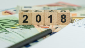 financial-tax-concept-as-number-2018-on-wooden-cube-block-on-pile-of-euro-banknotes-with-note-paper-and-pencil