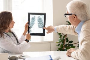 senior-patient-and-young-female-pulmonologist-pointing-at-x-ray-image-of-lungs